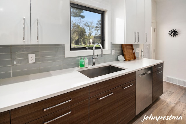 kitchen with stainless steel dishwasher, visible vents, wood finished floors, modern cabinets, and a sink