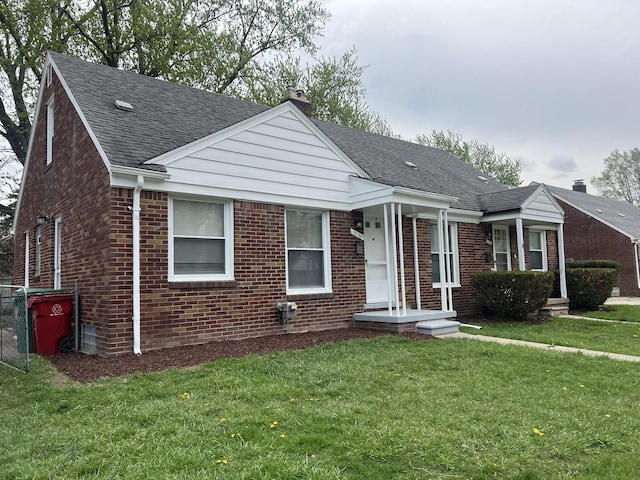 view of front facade featuring brick siding, roof with shingles, a chimney, and a front yard