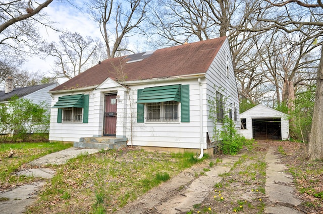 bungalow with a garage, an outdoor structure, driveway, and roof with shingles