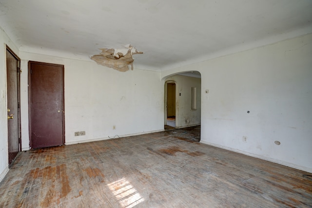 spare room with arched walkways, baseboards, and wood finished floors