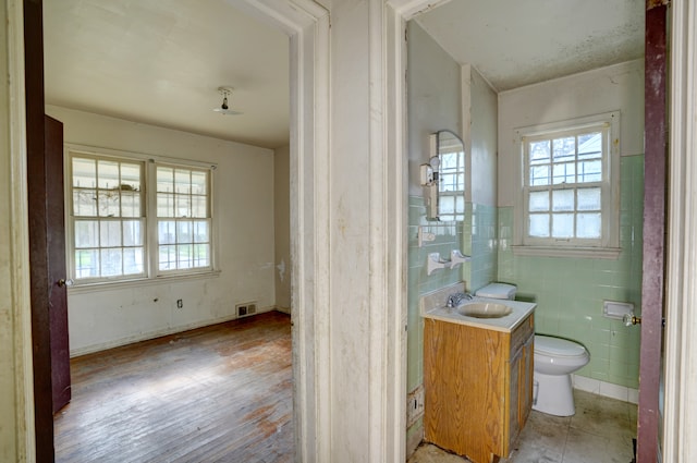 half bath with vanity, toilet, tile walls, wood finished floors, and visible vents