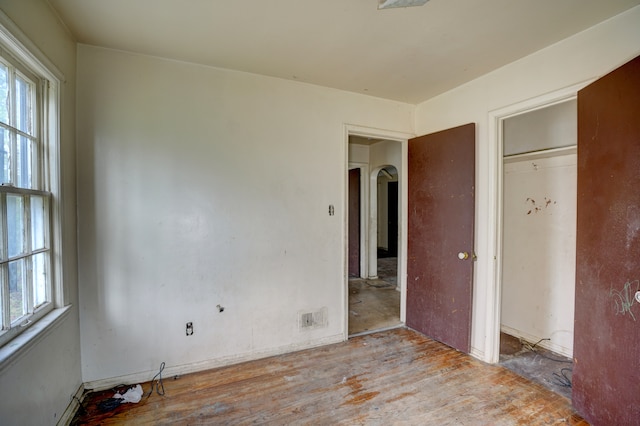 unfurnished bedroom with arched walkways, multiple windows, and wood finished floors