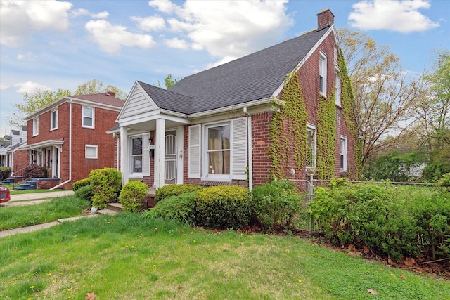 view of front of home with brick siding, a chimney, a front lawn, and a shingled roof