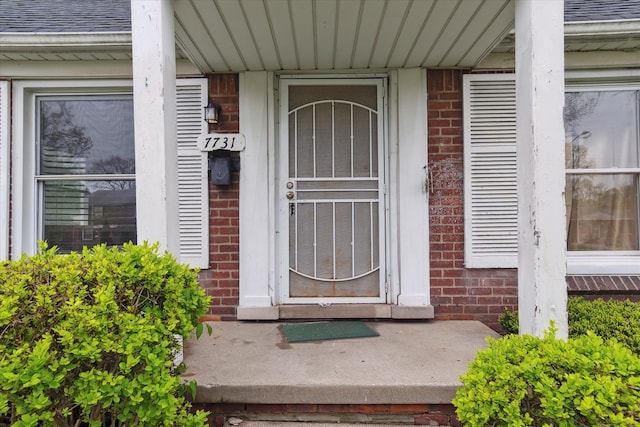 view of exterior entry featuring brick siding, roof with shingles, and a porch