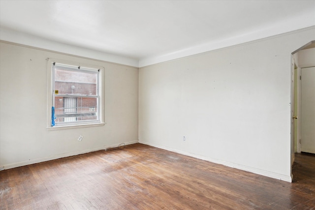 unfurnished room with wood finished floors, baseboards, and arched walkways