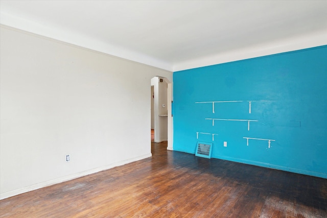 empty room with arched walkways, wood finished floors, and baseboards