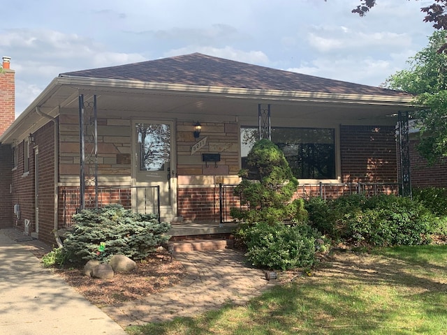 view of front facade with a porch, brick siding, and roof with shingles