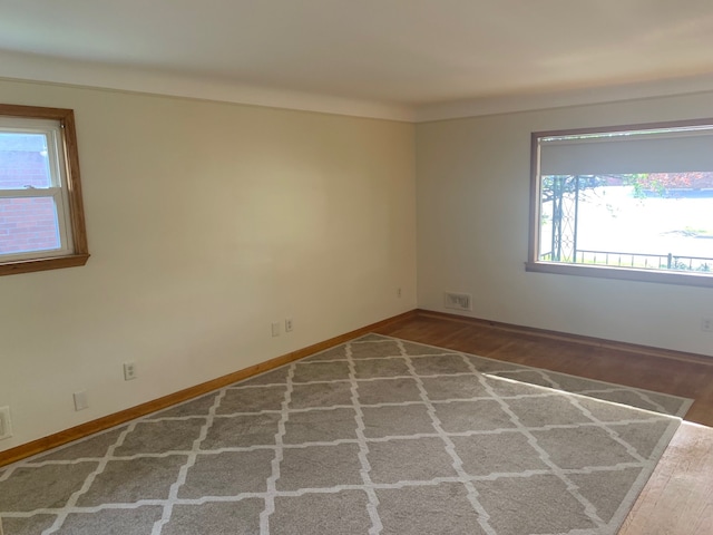 empty room featuring baseboards, wood finished floors, and visible vents