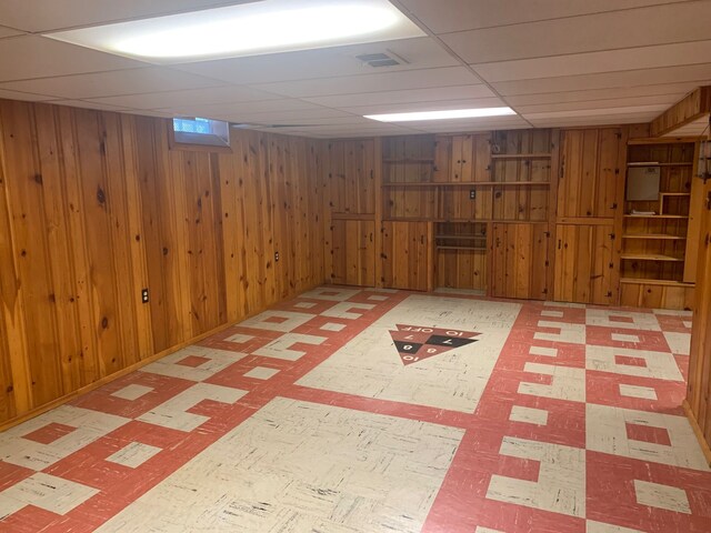 finished below grade area with wooden walls, tile patterned floors, and visible vents