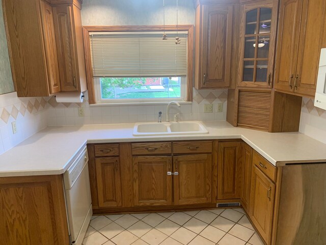 kitchen featuring brown cabinetry, backsplash, dishwasher, a sink, and glass insert cabinets