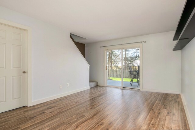unfurnished living room featuring stairs, baseboards, and wood finished floors