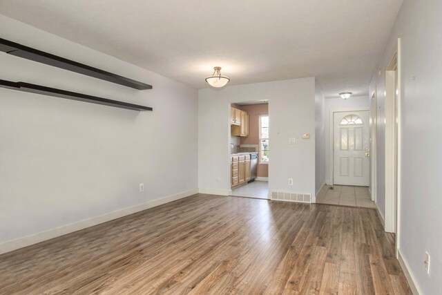unfurnished living room with visible vents, a sink, light wood-style flooring, and baseboards