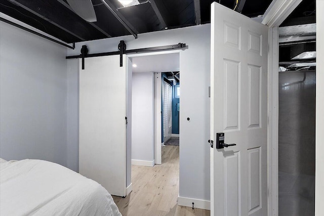 bedroom with light wood-style floors, baseboards, and a barn door