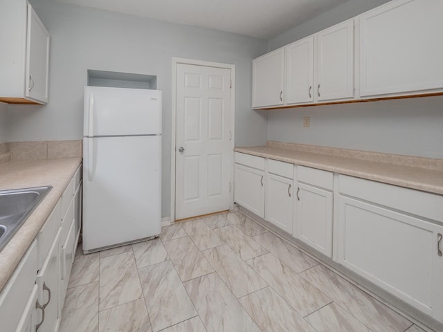 kitchen featuring a sink, light countertops, marble finish floor, freestanding refrigerator, and white cabinetry