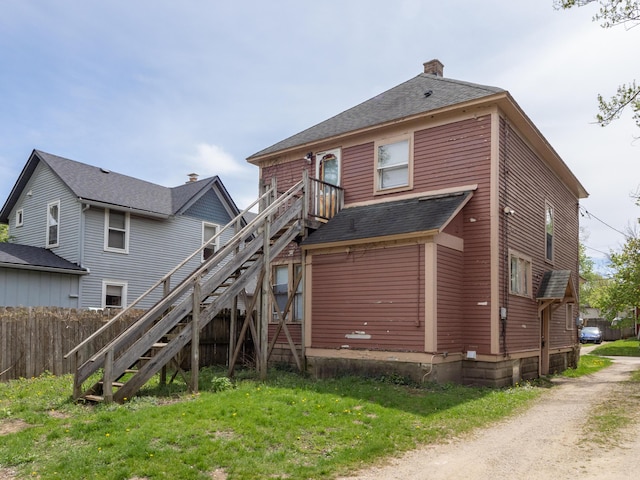 back of house featuring a chimney, roof with shingles, fence, a yard, and stairs