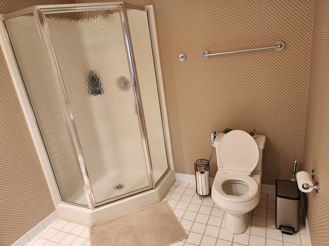 bathroom with toilet, tile patterned floors, baseboards, and a stall shower
