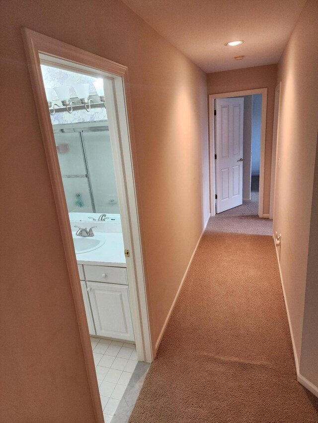 corridor featuring light colored carpet, a sink, and baseboards
