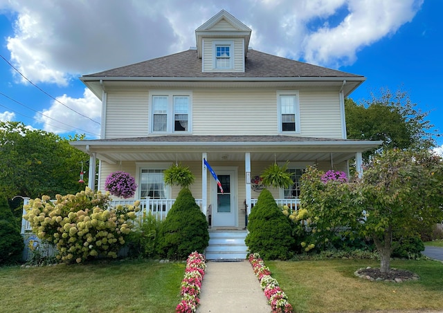 view of front of home featuring roof with shingles, covered porch, and a front lawn