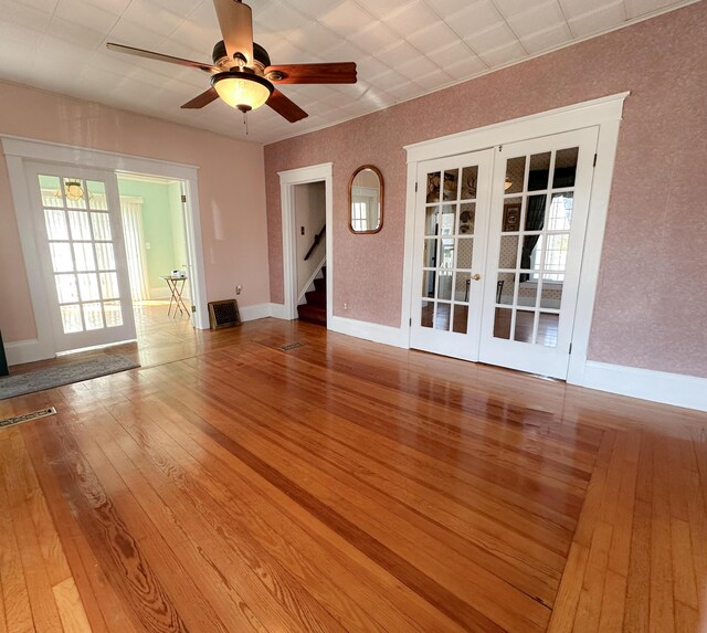 unfurnished living room featuring a ceiling fan, french doors, hardwood / wood-style flooring, stairway, and baseboards