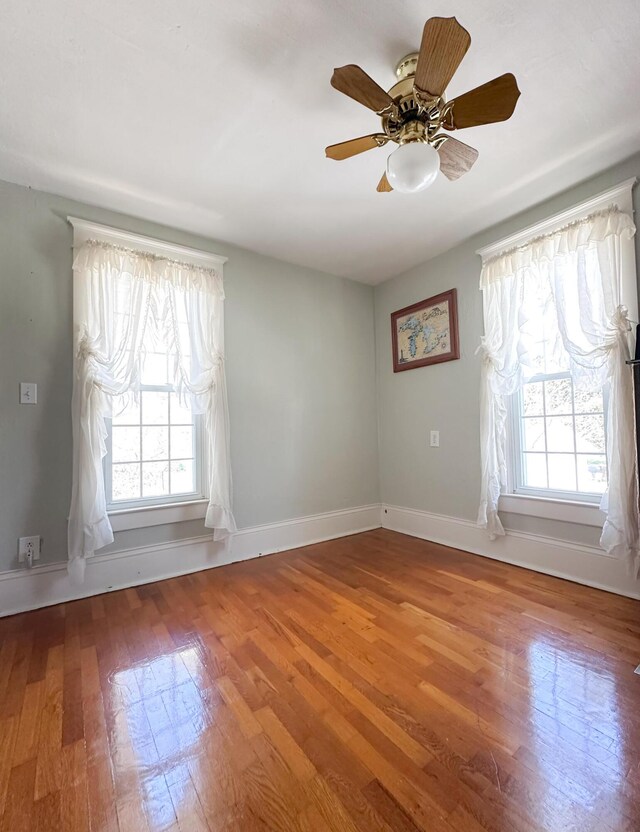 empty room featuring baseboards, plenty of natural light, a ceiling fan, and wood finished floors
