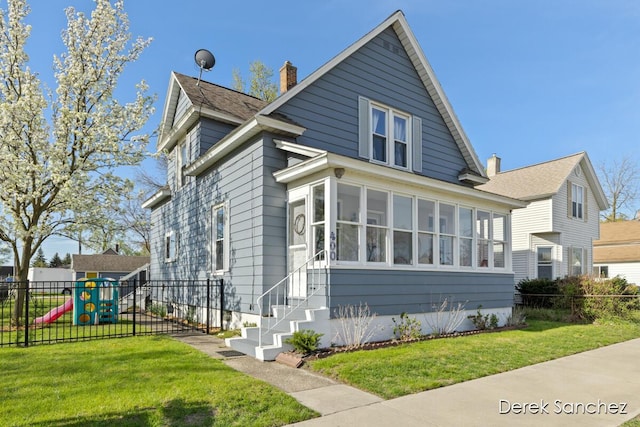 view of front facade featuring a chimney, a front yard, a sunroom, fence, and a playground