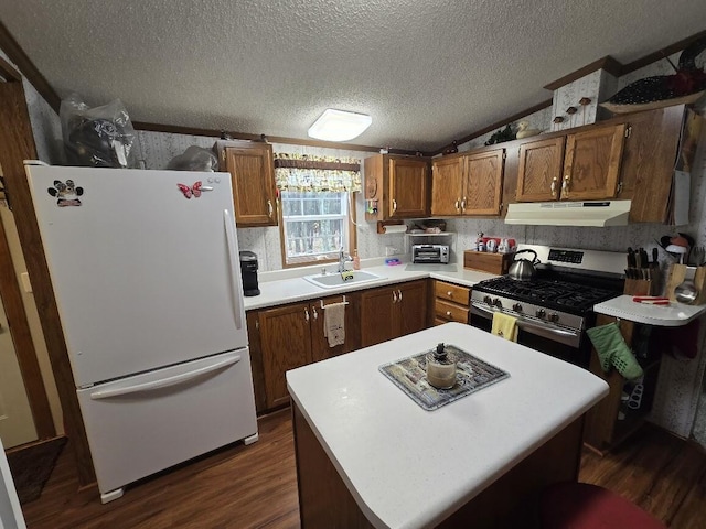 kitchen with freestanding refrigerator, stainless steel gas range, under cabinet range hood, a sink, and dark wood finished floors