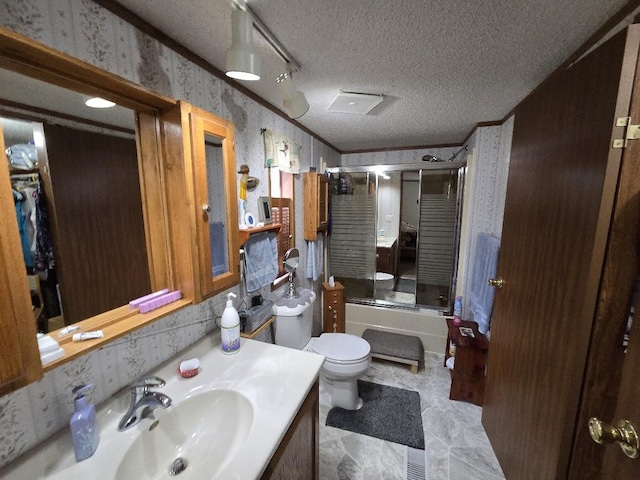 bathroom with a textured ceiling, vanity, toilet, shower / bath combination with glass door, and wallpapered walls
