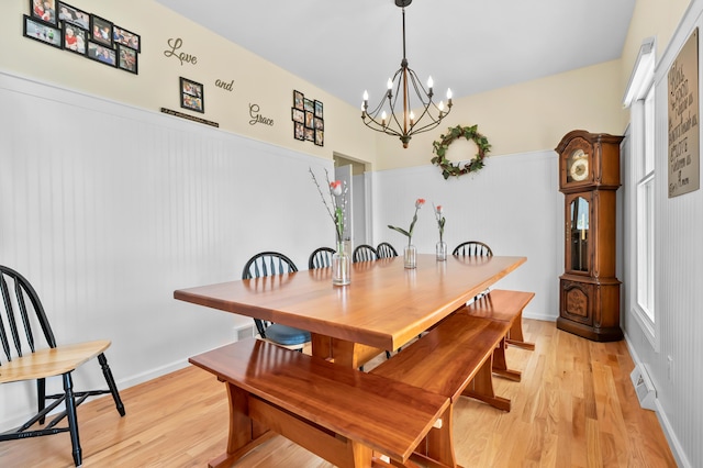 dining area with a wainscoted wall, visible vents, light wood-type flooring, and a notable chandelier