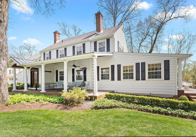 view of front facade with a porch, a ceiling fan, a front yard, and a chimney