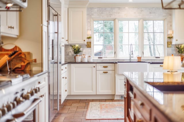 kitchen featuring decorative backsplash, dark countertops, high end white range, white cabinets, and a sink