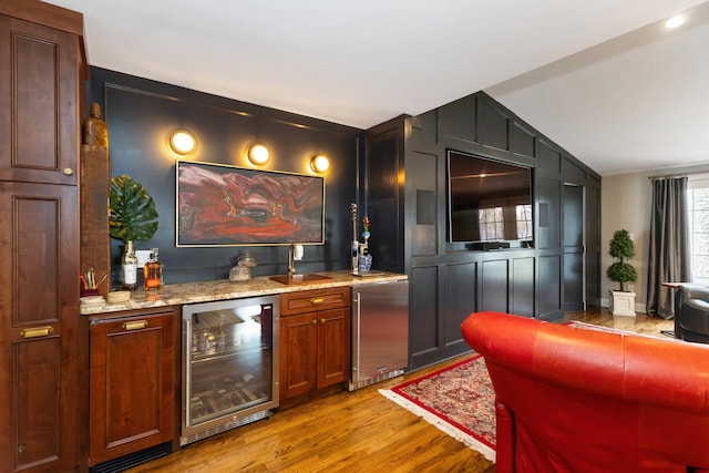 bar with a dry bar, vaulted ceiling, refrigerator, light wood finished floors, and beverage cooler