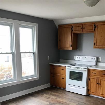 kitchen featuring brown cabinetry, electric range, wood finished floors, light countertops, and baseboards