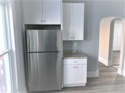 kitchen featuring freestanding refrigerator, baseboards, white cabinetry, arched walkways, and light wood finished floors
