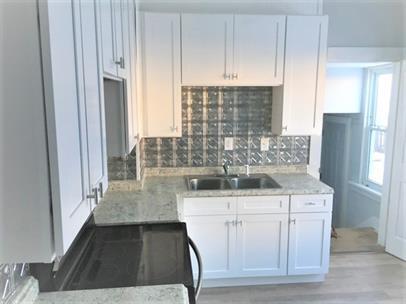 kitchen with light stone counters, a sink, white cabinetry, light wood-type flooring, and backsplash