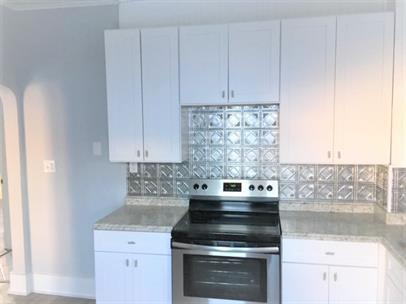 kitchen with stainless steel electric stove, white cabinets, and tasteful backsplash