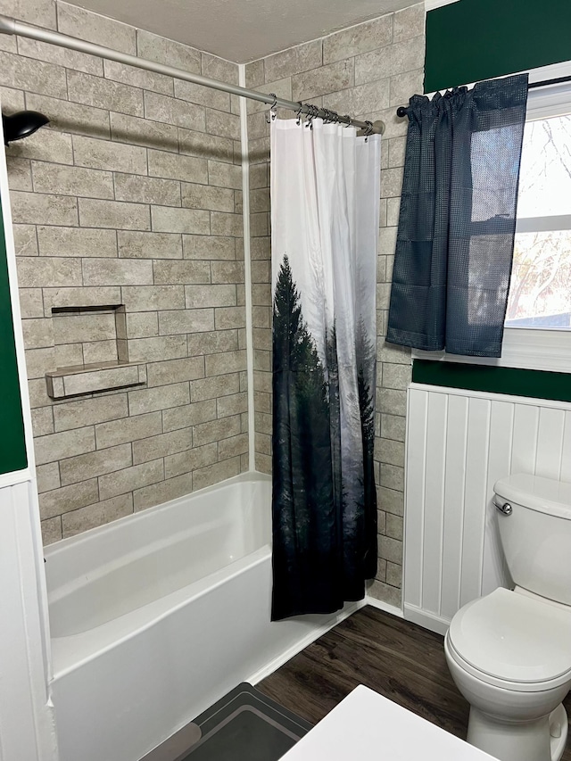 full bath featuring wood finished floors, shower / bath combination with curtain, toilet, and a wainscoted wall