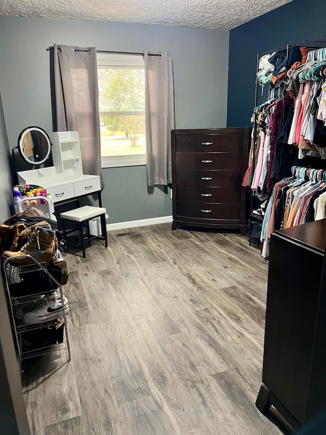 interior space featuring baseboards, a textured ceiling, wood finished floors, and visible vents
