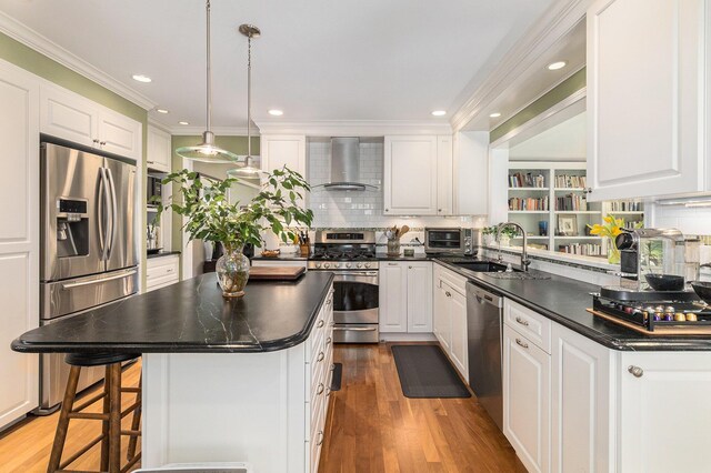 kitchen with wall chimney range hood, appliances with stainless steel finishes, dark countertops, a sink, and ornamental molding