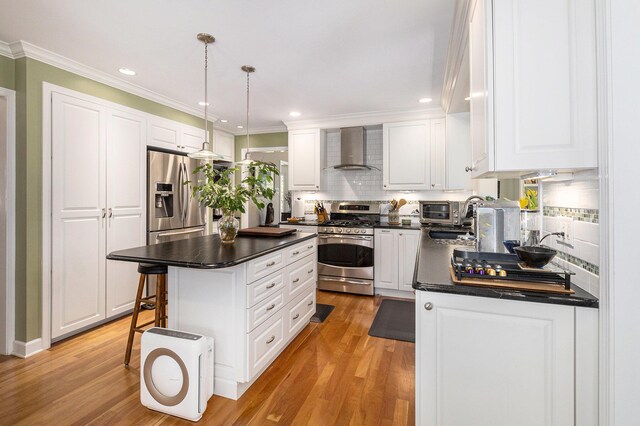 kitchen with dark countertops, ornamental molding, stainless steel appliances, and wall chimney exhaust hood