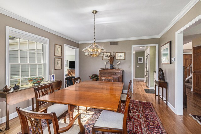 dining room with visible vents, wood finished floors, baseboards, a notable chandelier, and ornamental molding