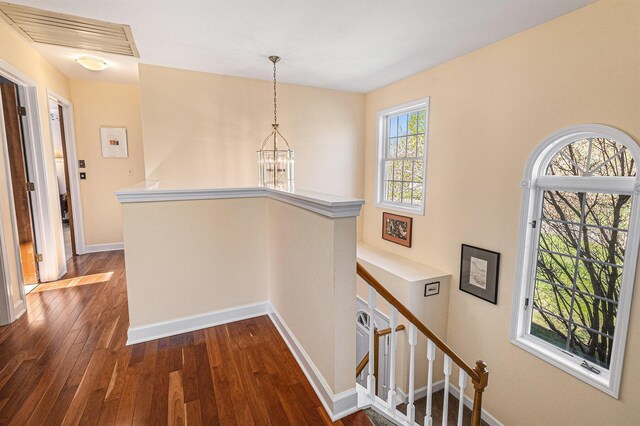hall with visible vents, an upstairs landing, dark wood finished floors, baseboards, and a notable chandelier