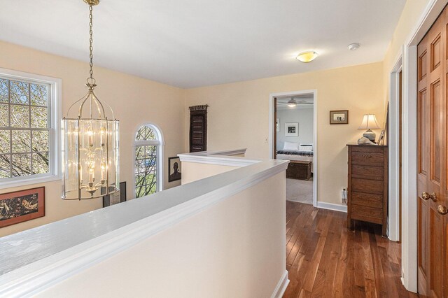 hall featuring baseboards, a notable chandelier, an upstairs landing, and dark wood-type flooring