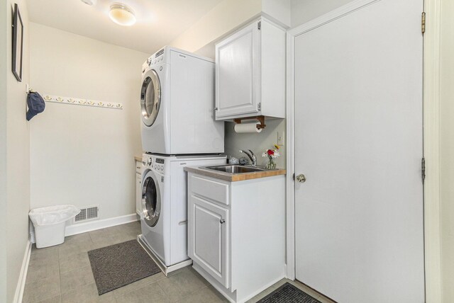 laundry room featuring visible vents, stacked washer and clothes dryer, baseboards, cabinet space, and light tile patterned floors