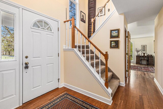 foyer entrance featuring stairs, baseboards, dark wood-style floors, and a healthy amount of sunlight