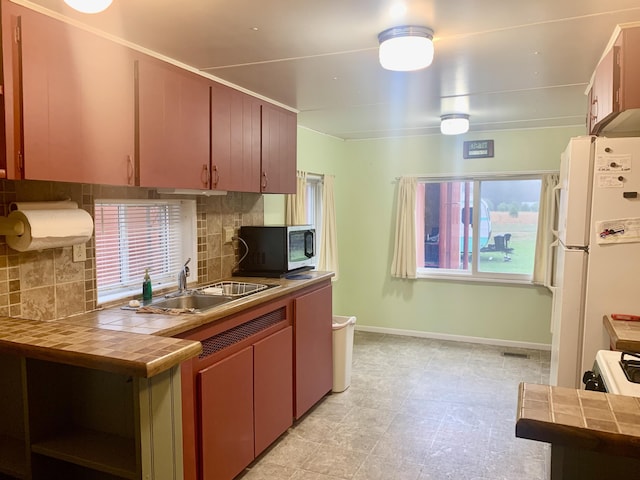 kitchen with a sink, freestanding refrigerator, tile countertops, baseboards, and backsplash