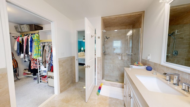 full bath featuring tile patterned flooring, vanity, tile walls, a spacious closet, and a stall shower