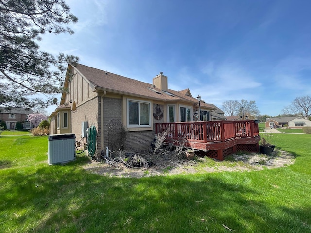 rear view of property featuring brick siding, a wooden deck, a chimney, cooling unit, and a yard