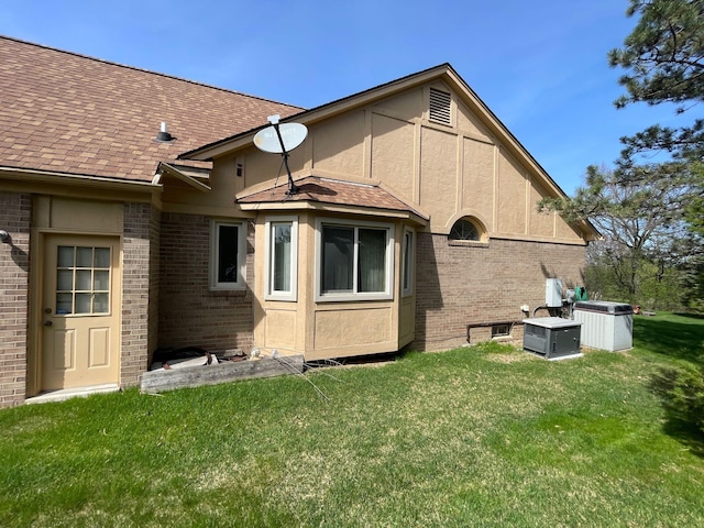 back of house featuring brick siding, a shingled roof, and a lawn