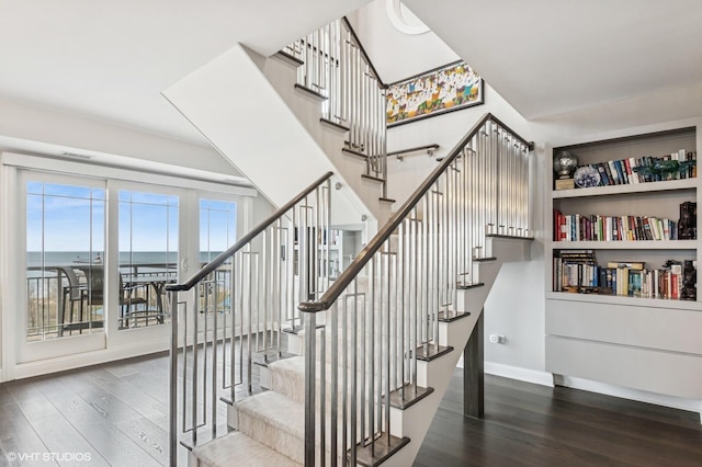 stairway with a water view, baseboards, and wood finished floors