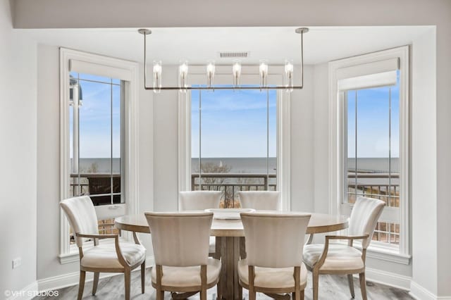 dining space with a water view, baseboards, visible vents, and wood finished floors